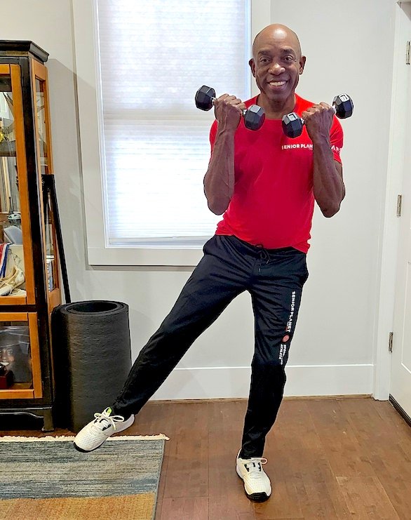 senior african american man exercising with weights, one leg raised
